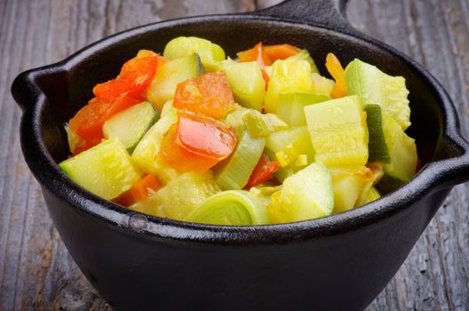 Vegetable Stew with Zucchini in Black Stew Pan closeup on Rustic Wooden background