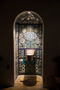 A nighttime view of a drinking water fountain in a tile-decorated niche.