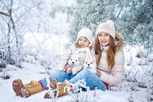 Young mother and daughter laughing for a walk in winter forest