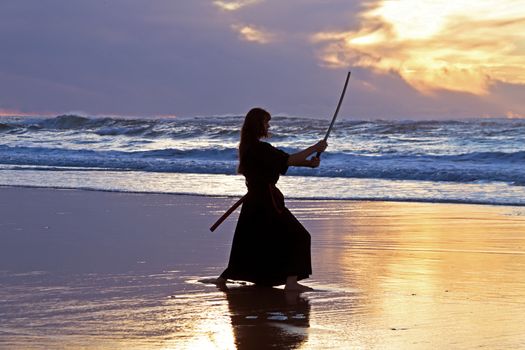 Young samurai women with Japanese sword(Katana) at sunset on the beach