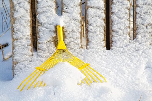 Yellow rake under snow in winter day