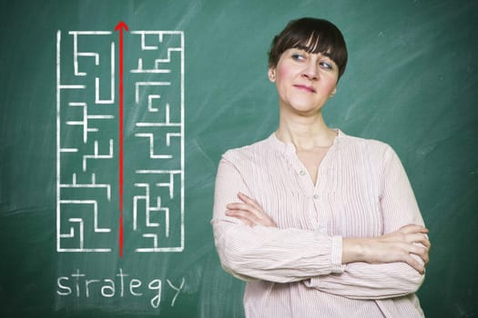 Woman smiles writes on a blackboard the concept of strategy