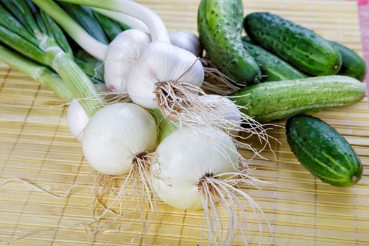 Still-life with onions garlic and green cucumbers on a table