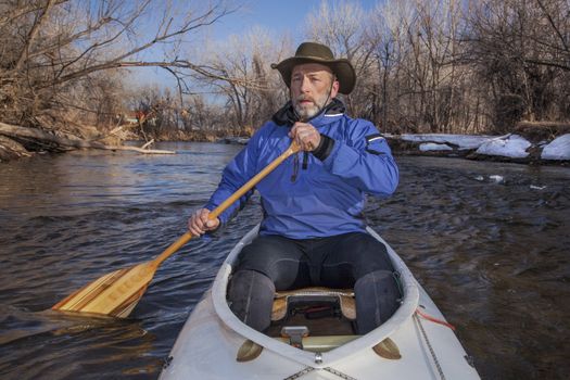 senior canoe paddler in a decked expedition canoe on the Cache la Poudre River, Fort Collins, Colorado, winter or early spring