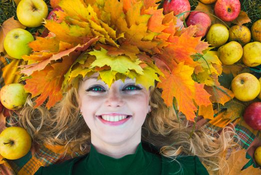 Woman in garland of maple leafs and apple crop. Autumn decorations