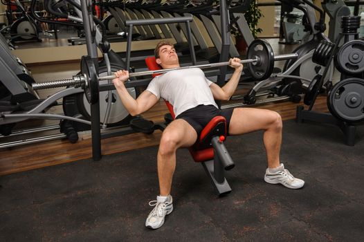 Handsome young man doing Barbell Incline Bench Press workout in gym