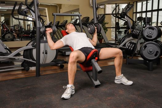 Handsome young man doing Dumbbell Incline Bench Press workout in gym
