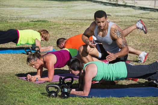 Muscular instructor with stopwatch helping students in fitness class