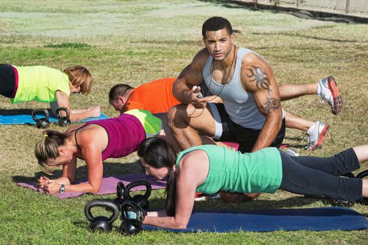 Instructor with tattoo helping bootcamp fitness students