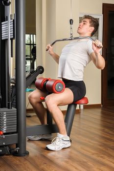 Handsome young man doing B lats pull-down workout in gym