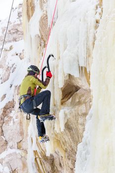 Young man climbing the ice using ice axe