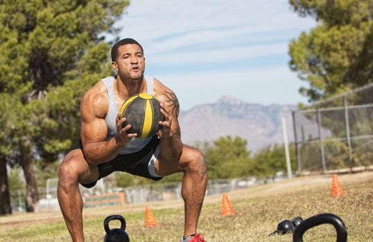 Strong African man squatting with medicine ball