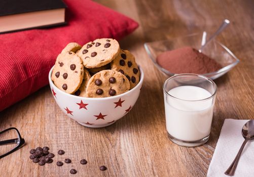 Closeup of chocolate chip cookies on stars bowl and milk glass over a wooden background