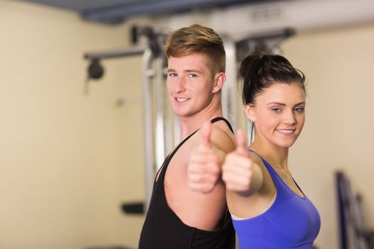 Side view portrait of a sporty couple gesturing thumbs up in the gym