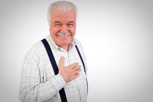 Sincere senior man with his hand on his heart looking at the camera with a warm friendly smile, upper body studio portrait on grey with copyspace
