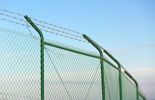 Mesh fence with barbed wire on a background of blue sky