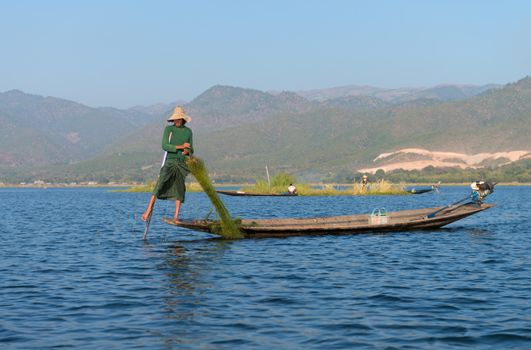 INLE LAKE, MYANMAR (BURMA) - 07 JAN 2014: Burmese fisherman in wooden boat leg row and use net to catch fish in Inle lake, Myanmar