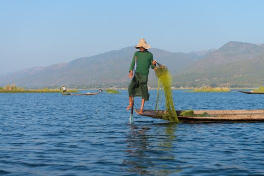 INLE LAKE, MYANMAR (BURMA) - 07 JAN 2014: Burmese fisherman in wooden boat leg row and use net to catch fish in Inle lake, Myanmar