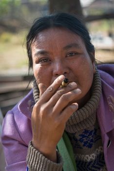 INLE LAKE, MYANMAR (BURMA) - 07 JAN 2014: Local Burmese Intha market woman smoke cheroot cigar with scale details on front. Selective focus on the eyes.