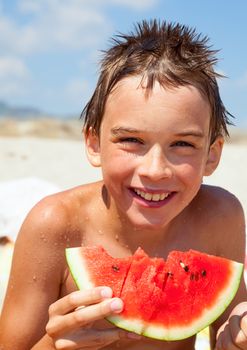 Happy boy eating watermelon on a beach