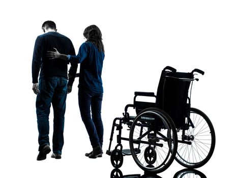 one man with woman walking away from wheelchair in silhouette studio on white background