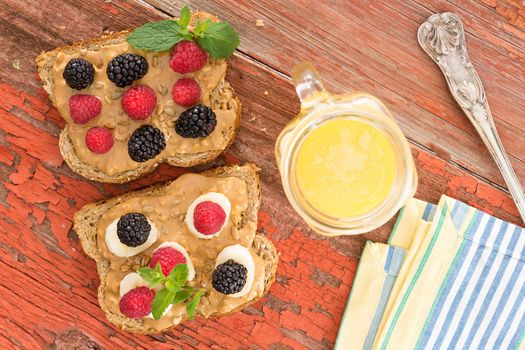 Overhead view of snacks on whole grain brown bread with fresh berries at a healthy country picnic laid out on a grungy old table with peeling paint alongside a jug of freshly squeezed orange juice