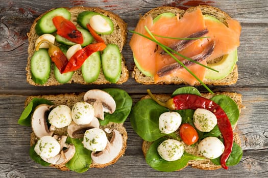 Four delicious open wholewheat sandwiches on a wooden picnic table topped with smoked salmon, avocado, mushrooms, cucumber , baby spinach and mozzarella cheese