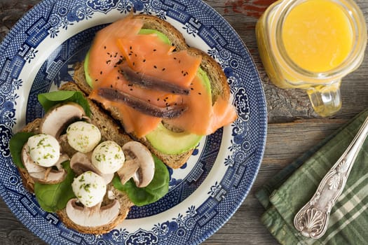 Delicious healthy sandwiches for a picnic lunch on two slices of wholewheat bread with smoked salmon, avocado, mushrooms and mozzarella cheese and a jug of fresh orange juice