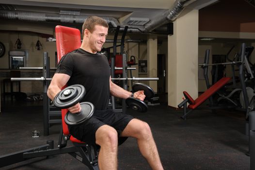 Handsome young man doing Dumbbell Biceps workout in gym. Motion blur at arms.