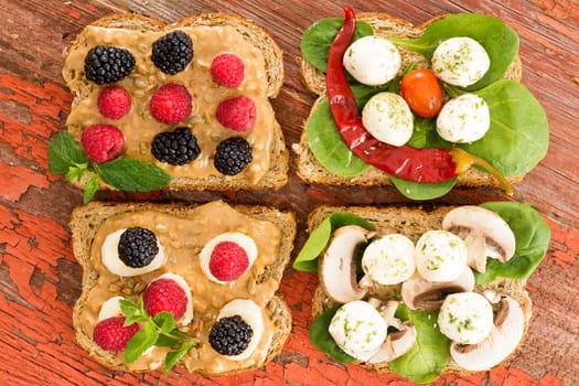 Healthy rustic picnic lunch with an assortment of wholewheat sandwiches topped with blackberries and raspberries, cheese, baby spinach, chili pepper and mushrooms, overhead view on a grungy wood table