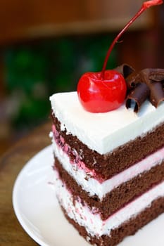 Chocolate cake with cherry on top on white plate