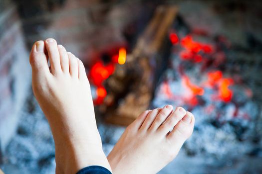 Woman's feet are heated in the fire in the fireplace with a brass 