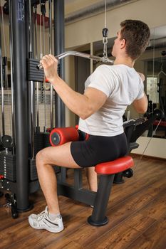 Handsome young man doing B lats pull-down workout in gym