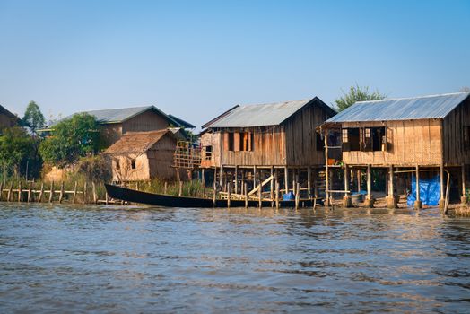 Traditional stilts wooden and bamboo houses and long boats of Intha people in water on Inle lake, Myanmar (Burma) 