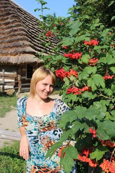 nice girk besides bush of clustered red and ripe guelder-rose besides an old rural house