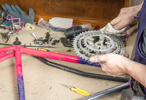 Hands of real bicycle mechanic cleaning chainring bike over workshop table in the repair process