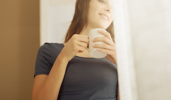 Beautiful woman with cup of coffee looking out of window. 