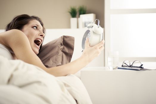Upset woman holding her alarm clock with an expression of fright