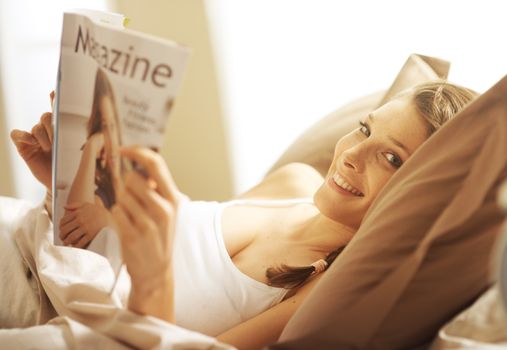 Woman lying in bed while reading a magazine