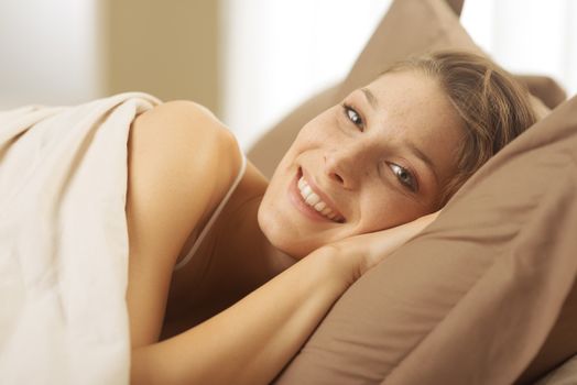 Young woman lying in bed and smiling at the camera 