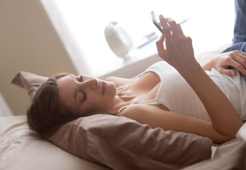 Young woman lying on the bed at home and receiving a text 