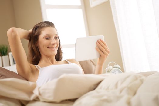 Woman enjoying with a digital tablet in bed in the morning, waking up.