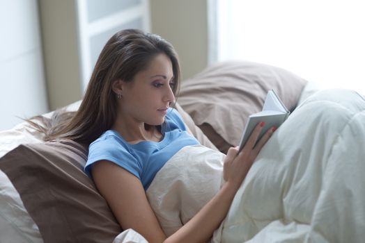 Young woman reading a book while lying on bed
