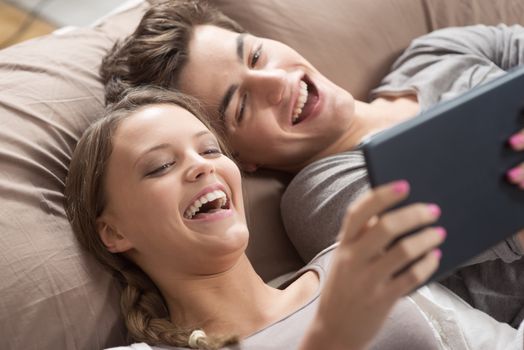 Happy young couple lying on the bed in a bedroom and using digital tablet.