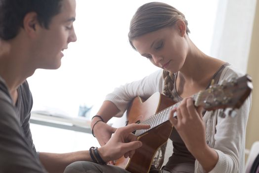 Young beautiful couple resting at home and playing guitar