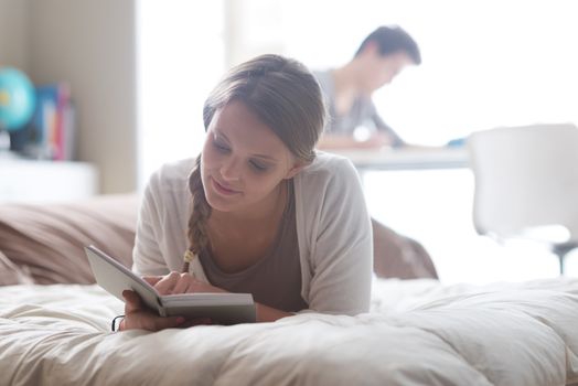 Beautiful girl reading a book while lying on bed. Boy studying on background
