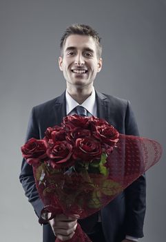 A handsome suitor holding out large bouquet of red roses 