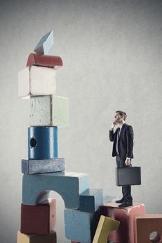 Businessman climbing a pile of wooden toy blocks.