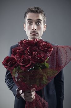 Shocked man holding out large bouquet of red roses 