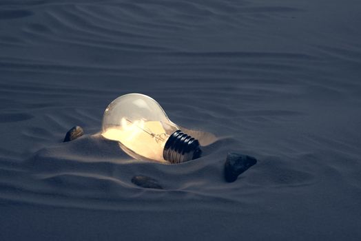 Lit light bulb in desert  dark setting.